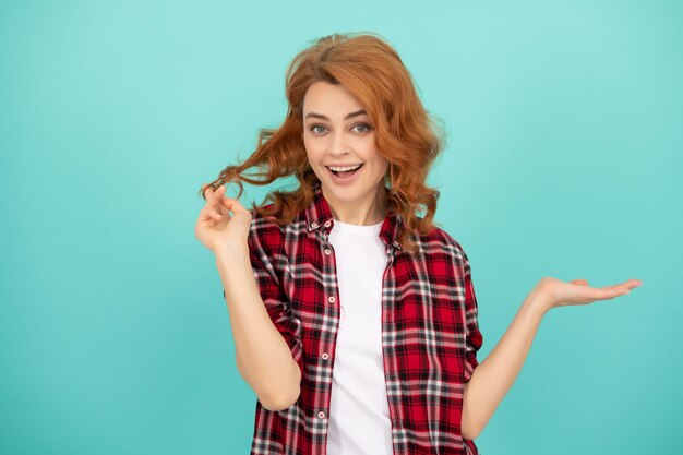 Szczęśliwa ruda kobieta z kręconymi włosami w kraciastej koszuli na co dzień przedstawiająca propozycję produktu w przestrzeni kopii produktu