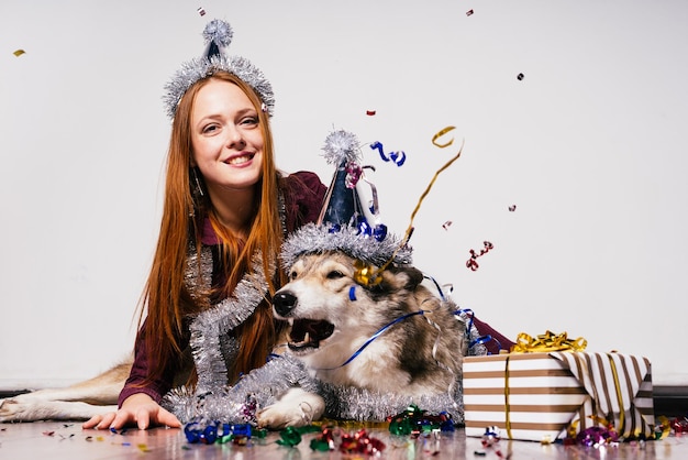 Szczęśliwa rudowłosa kobieta w czapce siedzi na podłodze ze swoim dużym psem i czeka na nowy rok i święta