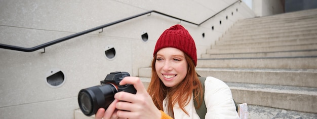 Zdjęcie szczęśliwa rudowłosa kobieta z miast i stylu życia robi zdjęcia, trzymając profesjonalny aparat cyfrowy