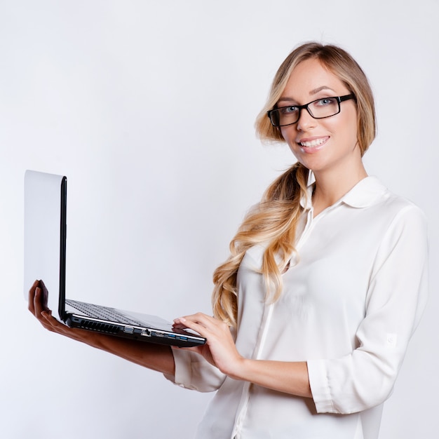Szczęśliwa śliczna kobieta pokazuje pustego laptopu ekran nad szarym tłem.