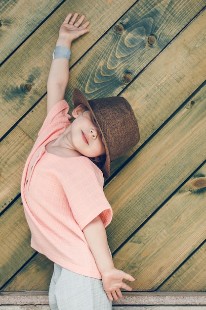 szczęśliwa śliczna mała dziewczynka w wiejskim stylu brązowy kapelusz i muślinowe ubrania w letni dzień na drewnianym backgro