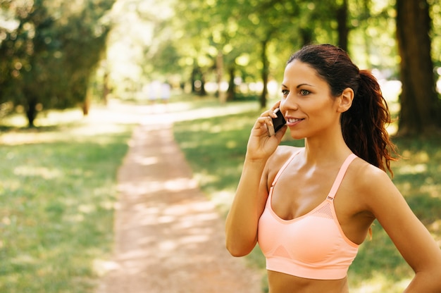 Szczęśliwa sporty kobieta opowiada na telefonie outdoors w parku