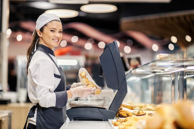 Szczęśliwa sprzedawczyni działu piekarni sprzedająca ciasto w supermarkecie