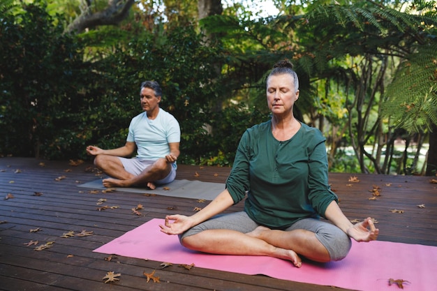Szczęśliwa starsza kaukaska para ćwicząca jogę, medytująca w słonecznym ogrodzie. zdrowy styl życia na emeryturze, spędzanie czasu w domu.