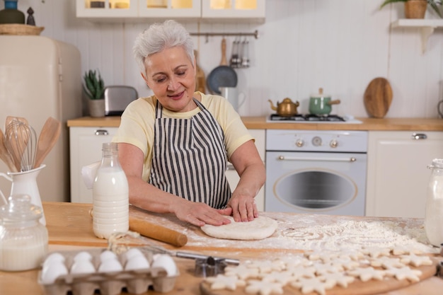 Szczęśliwa starsza kobieta gotująca w kuchni stylowa starsza, dojrzała siwowłosa babcia ugniata ciasto