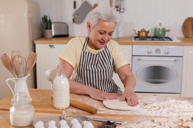Zdjęcie szczęśliwa starsza kobieta gotująca w kuchni stylowa starsza, dojrzała siwowłosa babcia ugniata ciasto