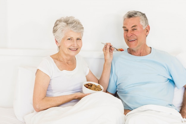 Szczęśliwa starsza kobieta karmi jej męża przy łóżkiem