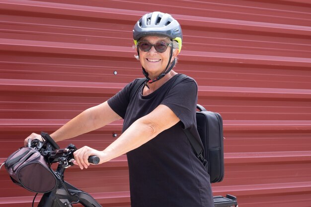 Szczęśliwa starsza kobieta rowerzysta w wycieczce na świeżym powietrzu w pobliżu czerwonego metalowego panelu zdrowy styl życia