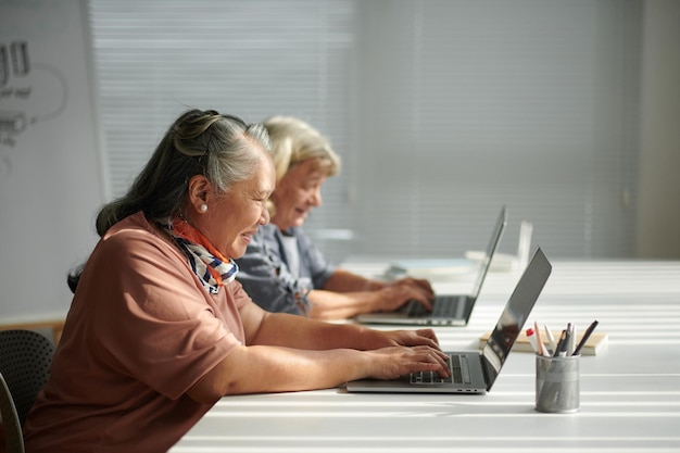 Szczęśliwa starsza kobieta uczy się pracy na laptopie w klasie dla początkujących