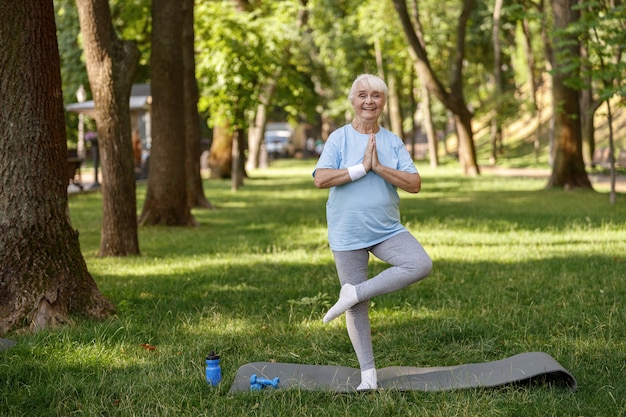 Szczęśliwa starsza pani w dresie robi drzewo pozuje ćwicząc asany jogi w parku