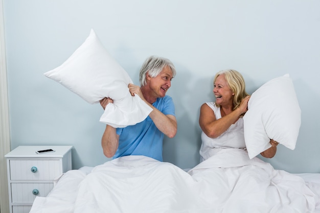 Zdjęcie szczęśliwa starsza para bawić się z poduszkami w sypialni