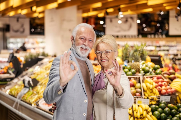 Szczęśliwa starsza para gestykuluje dobrze, stojąc w supermarkecie i uśmiechając się do kamery