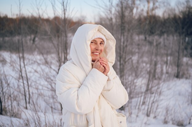 Szczęśliwa starsza starsza starsza kobieta w białej ciepłej odzieży wierzchniej, grając ze śniegiem w słoneczną zimę na zewnątrz