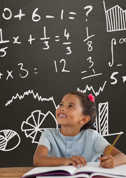 Szczęśliwa studentka przy stole, patrząc na szarą tablicę z grafiką edukacyjną i szkolną