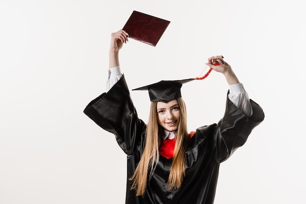 Szczęśliwa studentka w czarnej sukni dyplomowej i czapce podnosi dyplom magistra nad głową na białym tle Absolwentka kończy studia i świętuje osiągnięcia akademickie