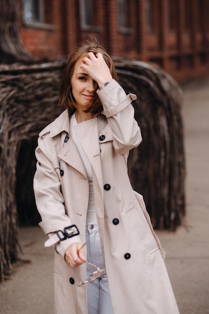 Szczęśliwa stylowa dziewczyna w szarym płaszczu spaceruje po mieście