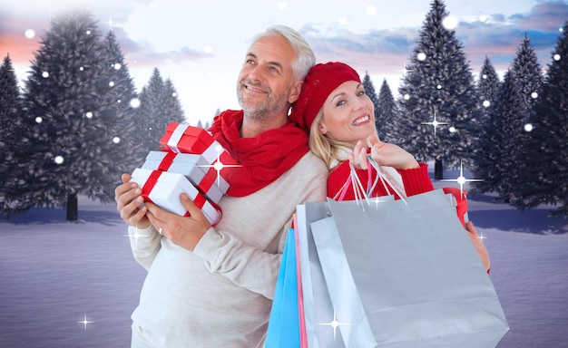 Szczęśliwa świąteczna para z prezentami i torbami przeciw śnieżnemu krajobrazowi z jodłami