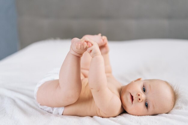 Szczęśliwa, szczera, urocza dziewczynka trzymająca małe stopy w rękach leżąca sama na przytulnym łóżku bawiąca się.
