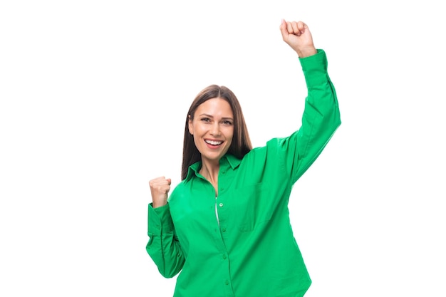 Szczęśliwa szczupła europejska młoda brunetka kobieta z makijażem w zielonej koszuli tańcząca na białym tle z
