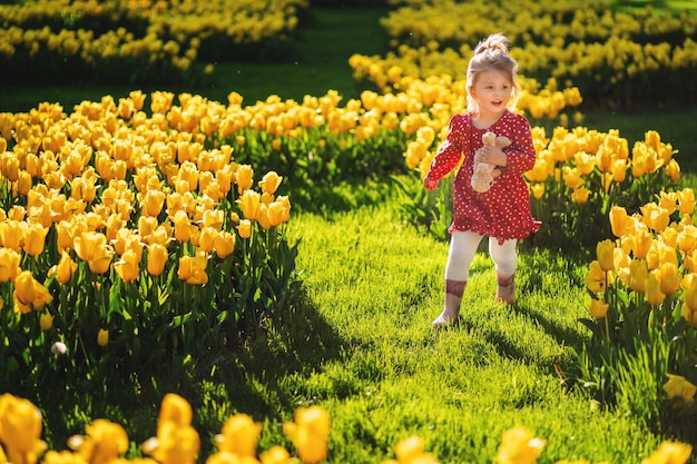 Szczęśliwa Trzylatka Biegnie Przez Trawnik Z Kwitnącymi żółtymi Tulipanami