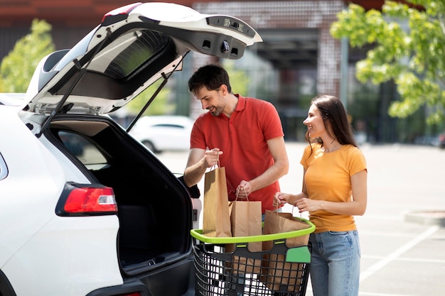 Szczęśliwa, tysiącletnia para ładująca zakupy po zakupach do bagażnika samochodu