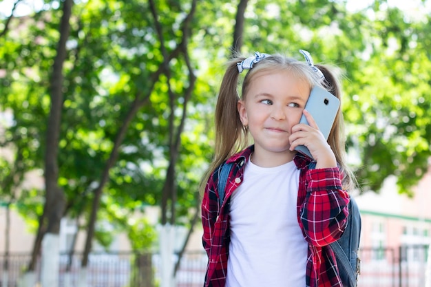 Szczęśliwa Uczennica Z Plecakiem Rozmawia Przez Telefon Na Ulicy. W Białej Koszulce I Koszuli W Kratę