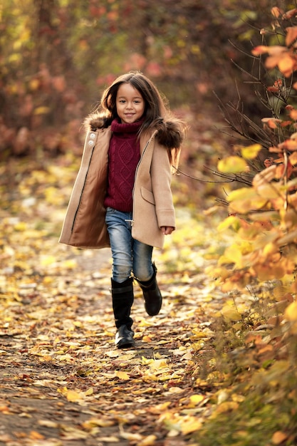 Szczęśliwa urocza dziewczynka biega w jesiennym parku. szczęśliwe dzieciństwo