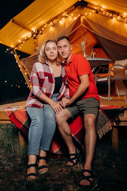 Szczęśliwa urocza para relaksująca się w glampingu wieczorem w pobliżu przytulnego ogniska Luksusowy namiot kempingowy do rekreacji na świeżym powietrzu i rekreacji Koncepcja stylu życia