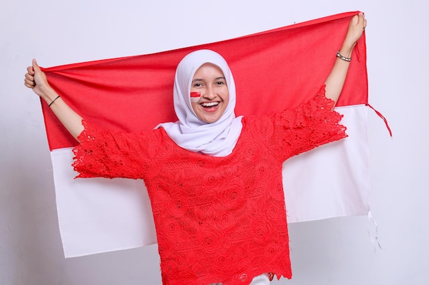 Szczęśliwa uśmiechnięta indonezyjska kobieta świętuje Dzień Niepodległości Indonezji, trzymając indonezyjską flagę