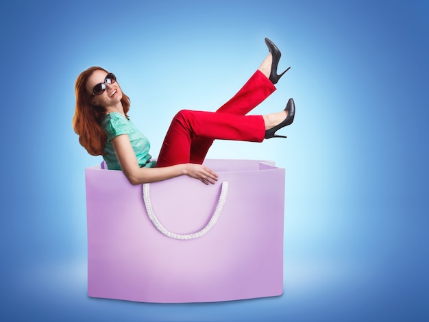 Szczęśliwa uśmiechnięta kobieta leżąca w torbie na zakupy na niebieskim tle