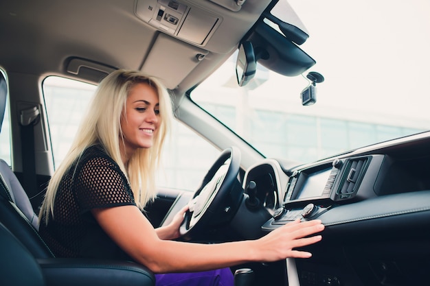 Szczęśliwa Uśmiechnięta Kobieta Raduje Się W Nowym Drogim Zakupie W Auto Salonie. Piękny Klient Siedzi Na Drzwiach Białego Składanego Górnego Samochodu.