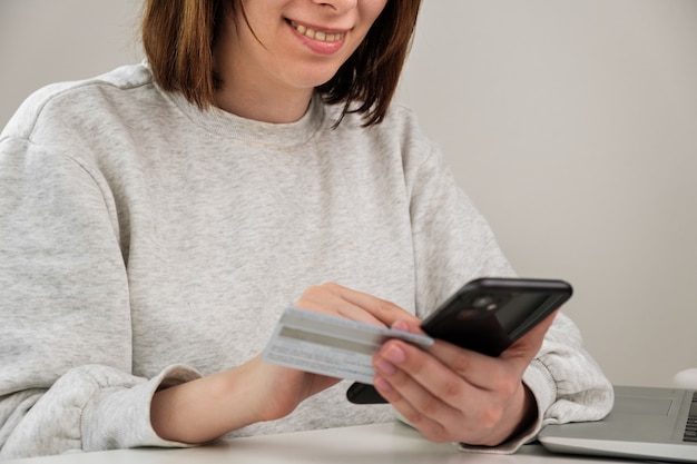 Szczęśliwa uśmiechnięta kobieta trzymająca kartę kredytową i płacąca telefonem komórkowym przez klienta robi zakupy online