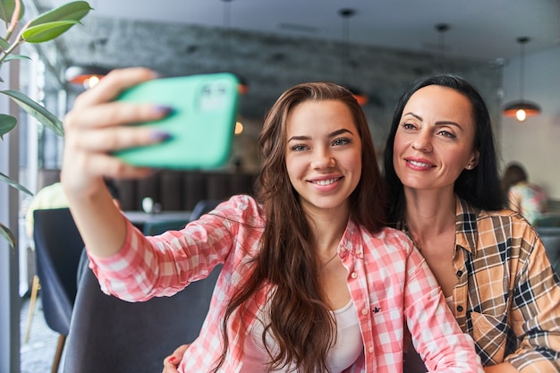 Szczęśliwa uśmiechnięta matka i radosna młoda córka robienie selfie zdjęcie aparatem telefonu i dobrą zabawę razem w kawiarni