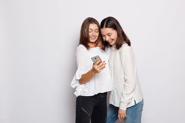 Szczęśliwa uśmiechnięta młoda kobieta pokazująca zdjęcia na telefonie komórkowym swojemu przyjacielowi