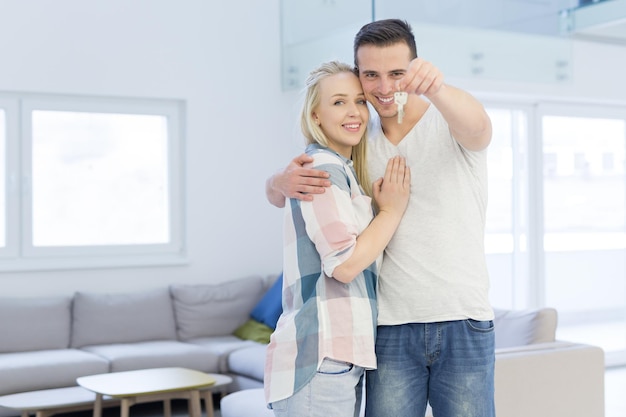 Szczęśliwa uśmiechnięta młoda para przytulająca się, pokazująca klucze do ich nowego domu