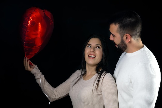 Szczęśliwa uśmiechnięta młoda para trzymająca czerwony balon w kształcie serca