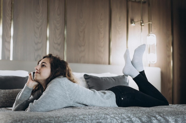 Szczęśliwa uśmiechnięta nastolatka rozmawia przez telefon leżąc na łóżku