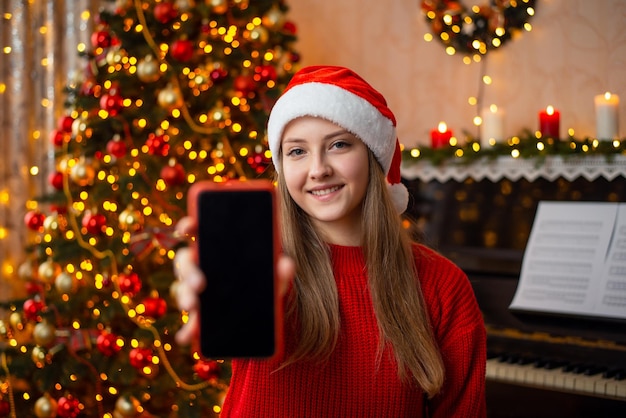 Szczęśliwa uśmiechnięta nastoletnia dziewczyna pokazuje ekran telefon komórkowy