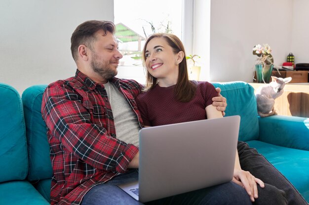 Szczęśliwa uśmiechnięta para rodzinna w średnim wieku patrząca razem na ekran laptopa