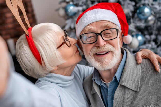 Zdjęcie szczęśliwa uśmiechnięta para seniorów w kapeluszach robiąca sobie selfie w domu