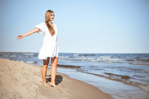 Szczęśliwa uśmiechnięta piękna kobieta spaceruje po plaży oceanu z otwartymi ramionami.