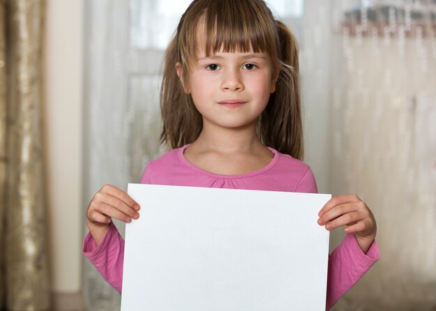 Szczęśliwa uśmiechnięta śliczna dziecko dziewczyna trzyma biel kopii przestrzeni prześcieradło rysunku papier. Edukacja artystyczna, kreatywność, koncepcja reklamy.