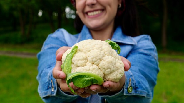 Szczęśliwa wegetariańska gospodyni domowa trzyma świeży kalafior w swoim organicznym ogrodzie i uśmiecha się rolnik z kalafiorem podczas żniw Zdrowa żywność wegetariańska dieta warzywna z bliska