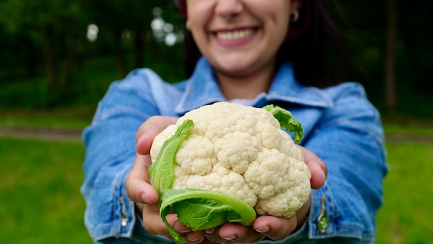 Szczęśliwa wegetariańska gospodyni domowa trzyma świeży kalafior w swoim organicznym ogrodzie i uśmiecha się rolnik z kalafiorem podczas żniw Zdrowa żywność wegetariańska dieta warzywna z bliska