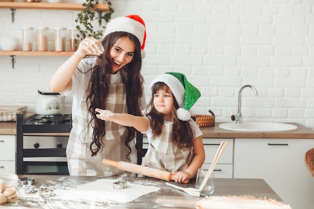 Szczęśliwa wesoła mama i dziecko w czapkach Świętego Mikołaja gotują świąteczne ciasteczka w kuchni Nowy Rok i Święta