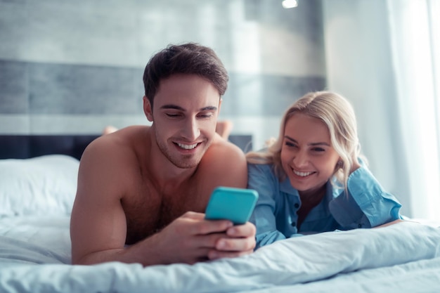 Szczęśliwa wesoła para śmiejąca się podczas oglądania śmiesznych filmów relaksujących się w łóżku w domu