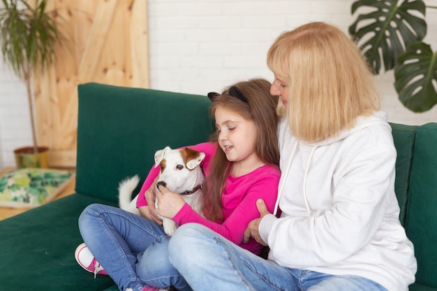 Szczęśliwa wnuczka i babcia siedzą na kanapie z psem jack russell terrierem, przytula się do babci