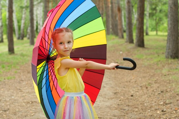 Zdjęcie szczęśliwa zabawna dziewczyna trzymająca tęczowy parasol urocza szczęśliwa uczennica bawiąca się w deszczowym letnim parku