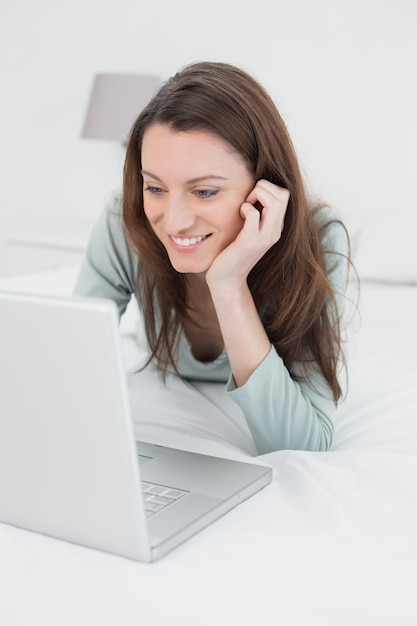 Szczęśliwa zrelaksowana przypadkowa kobieta używa laptop w łóżku