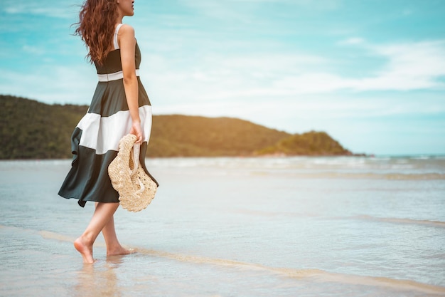 Szczęśliwe azjatyckie kobiety z trzymającym kapelusz stoją, aby otrzymać wiatr i cieszyć się życiem na wakacjach na plaży. plaża, lato, styl windy, pozytywny nastrój, podróże, koncepcja relaksu.